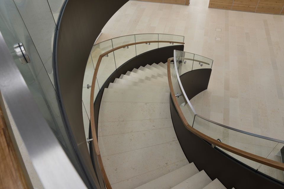 Geschwungene Treppe mit hellen Stufen und dunkelbraunen Wänden, Holzhandläufen und Glaspaneelen.