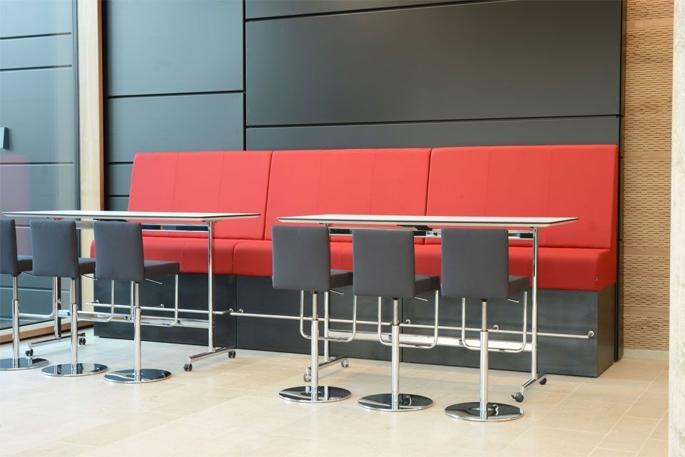 Rote und schwarze Sitznischen mit Edelstahltischen und schwarzen Hockern in einem modernen Interieur.