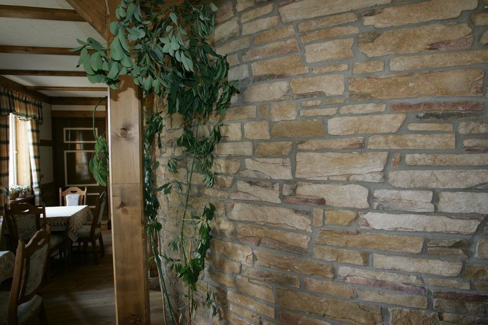 Steinmauer mit rankenden grünen Pflanzen und Holzpfosten; im Hintergrund das Esszimmer.