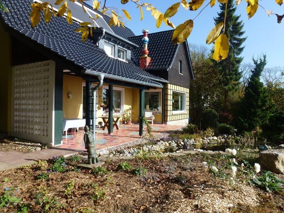 Haus mit dunklem Dach, Veranda und Garten an einem sonnigen Tag.