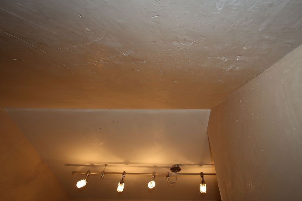 Ecke zwischen Decke und Wand, mit darüberliegender Schienenbeleuchtung und einer strukturierten weißen Oberfläche.