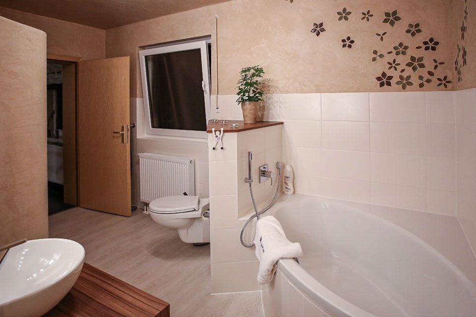 Badezimmer mit weißer Badewanne, Toilette und Waschbecken. Beige Wände mit Blumenmuster.