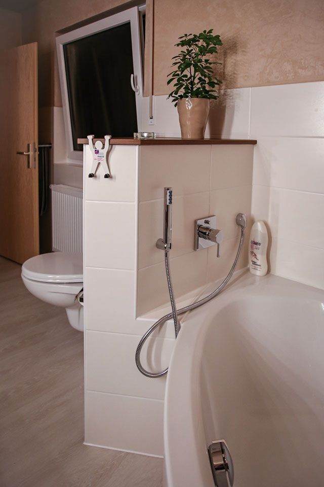 Badezimmerinterieur mit Badewanne, Toilette und Duscharmaturen. Auf einem Sims steht eine Pflanze.