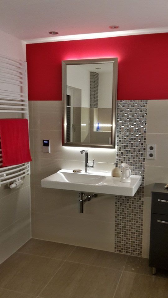 Modernes Badezimmer mit roter Wand und rechteckigem Spiegel über einem weißen Waschbecken.