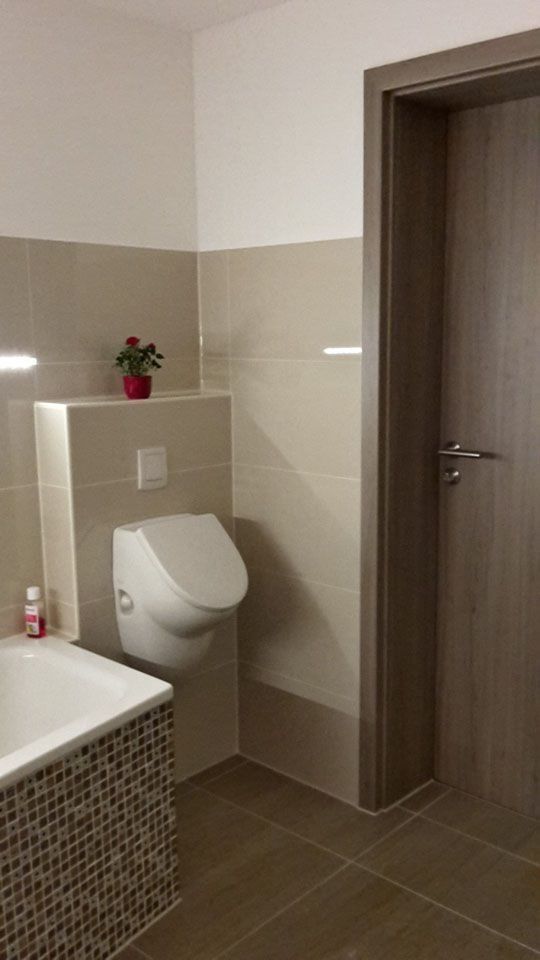 Modernes Badezimmer mit wandhängendem WC, beigefarbenen und weißen Fliesen und einer Holztür.