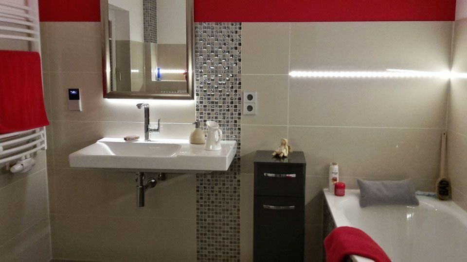 Modernes Badezimmer mit roten Akzenten, weißem Waschbecken und eingebauter Badewanne.