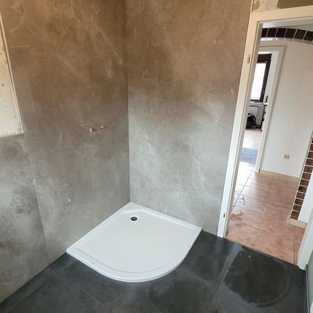 Im Bau befindliche Duschkabine mit grauen Wänden, weißem Boden und Türöffnung.