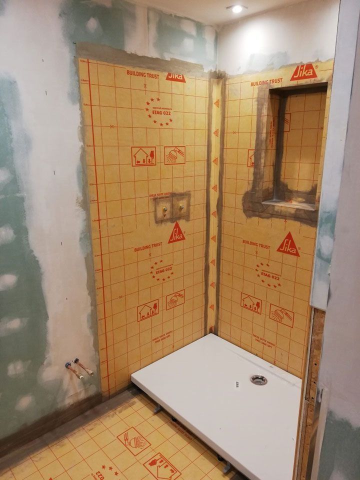 Duschkabine im Bau, mit gelber wasserdichter Rückwand, weißer Duschwanne und Sanitärarmaturen.