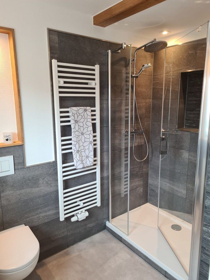 Modernes Badezimmer mit gefliester Dusche, Handtuchwärmer und Toilette.