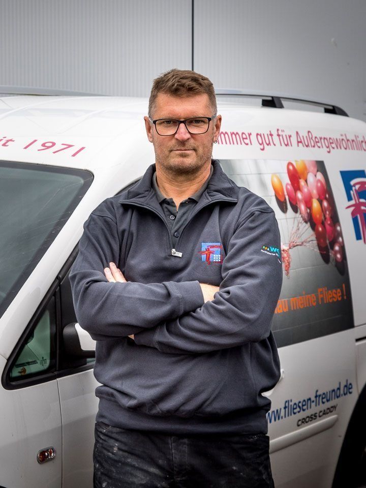 Mann in grauem Hemd mit verschränkten Armen steht vor einem Lieferwagen mit Firmenlogo.