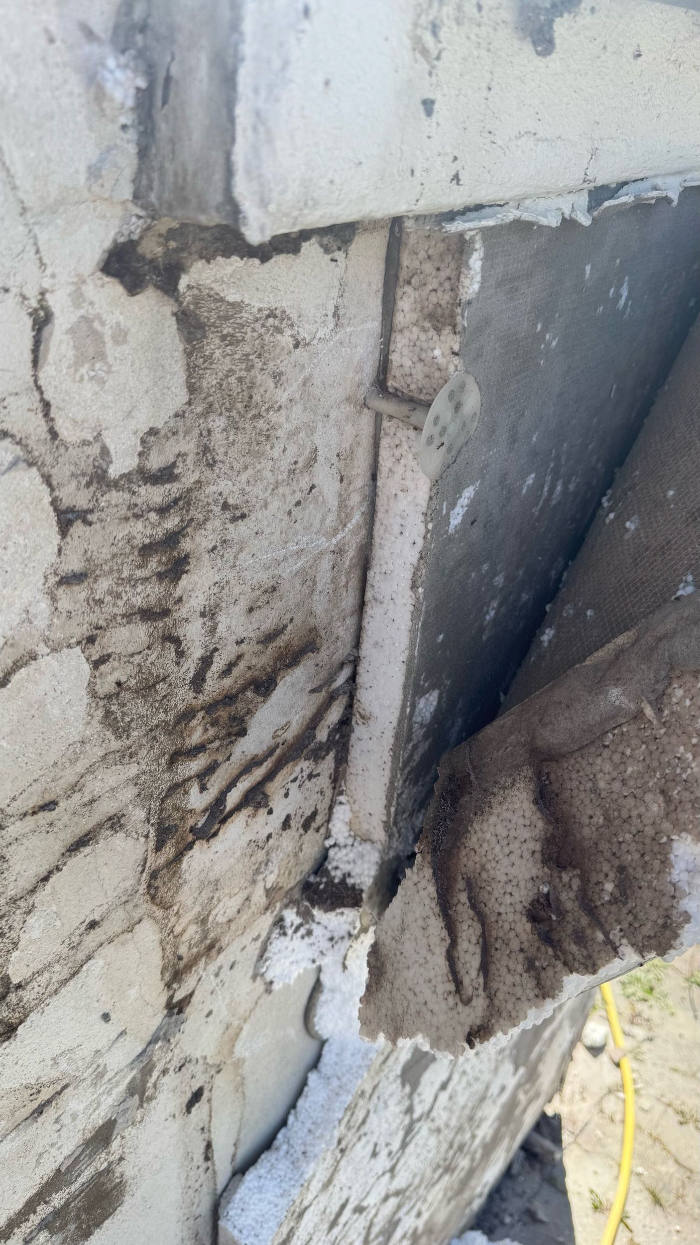 Nahaufnahme einer beschädigten Betonkonstruktion mit dunklen Streifen und sichtbaren Lücken.