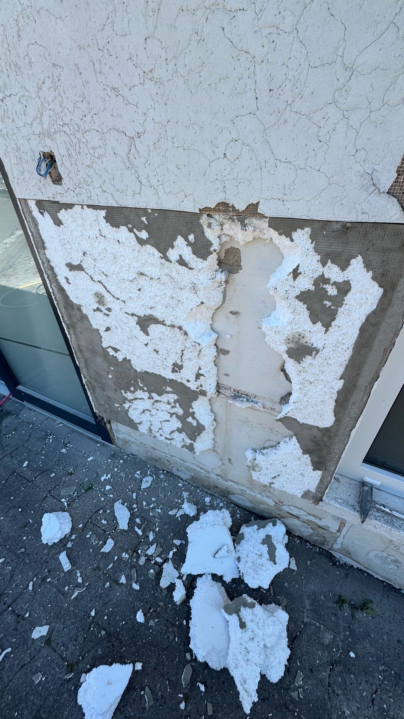 Beschädigte Außenwand mit abblätterndem Putz und darunterliegendem Schutt.