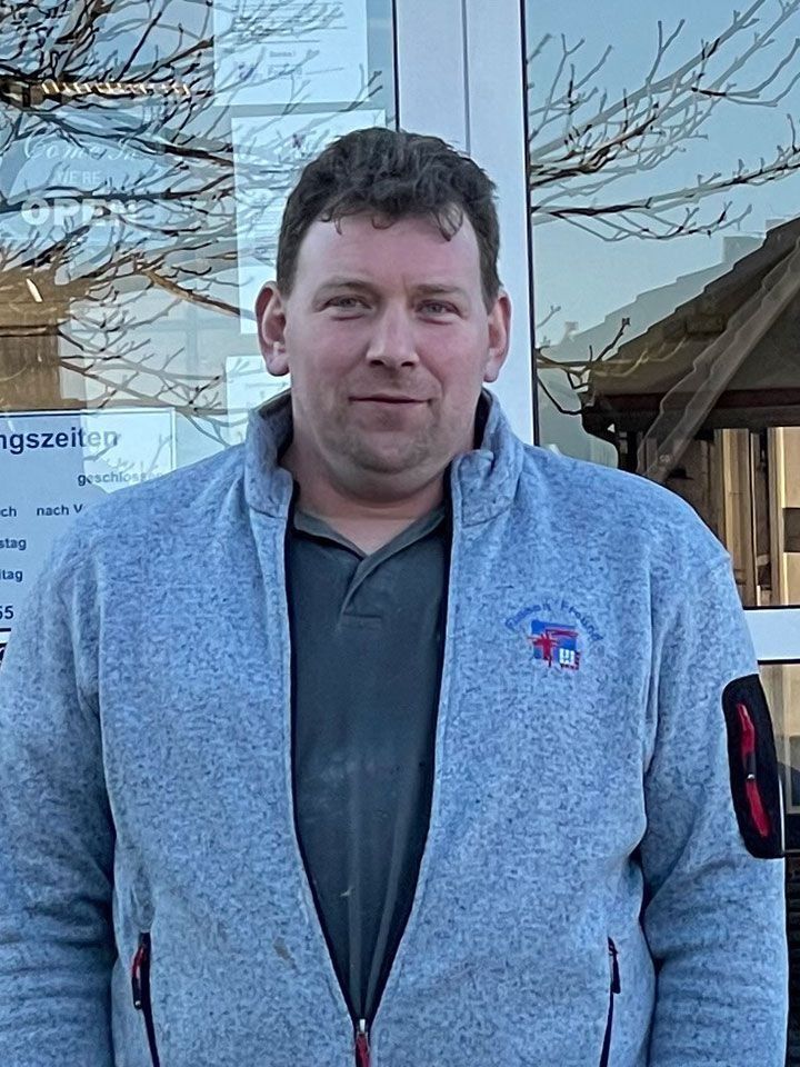 Mann in grauer Fleecejacke, der vor einer Glastür steht.