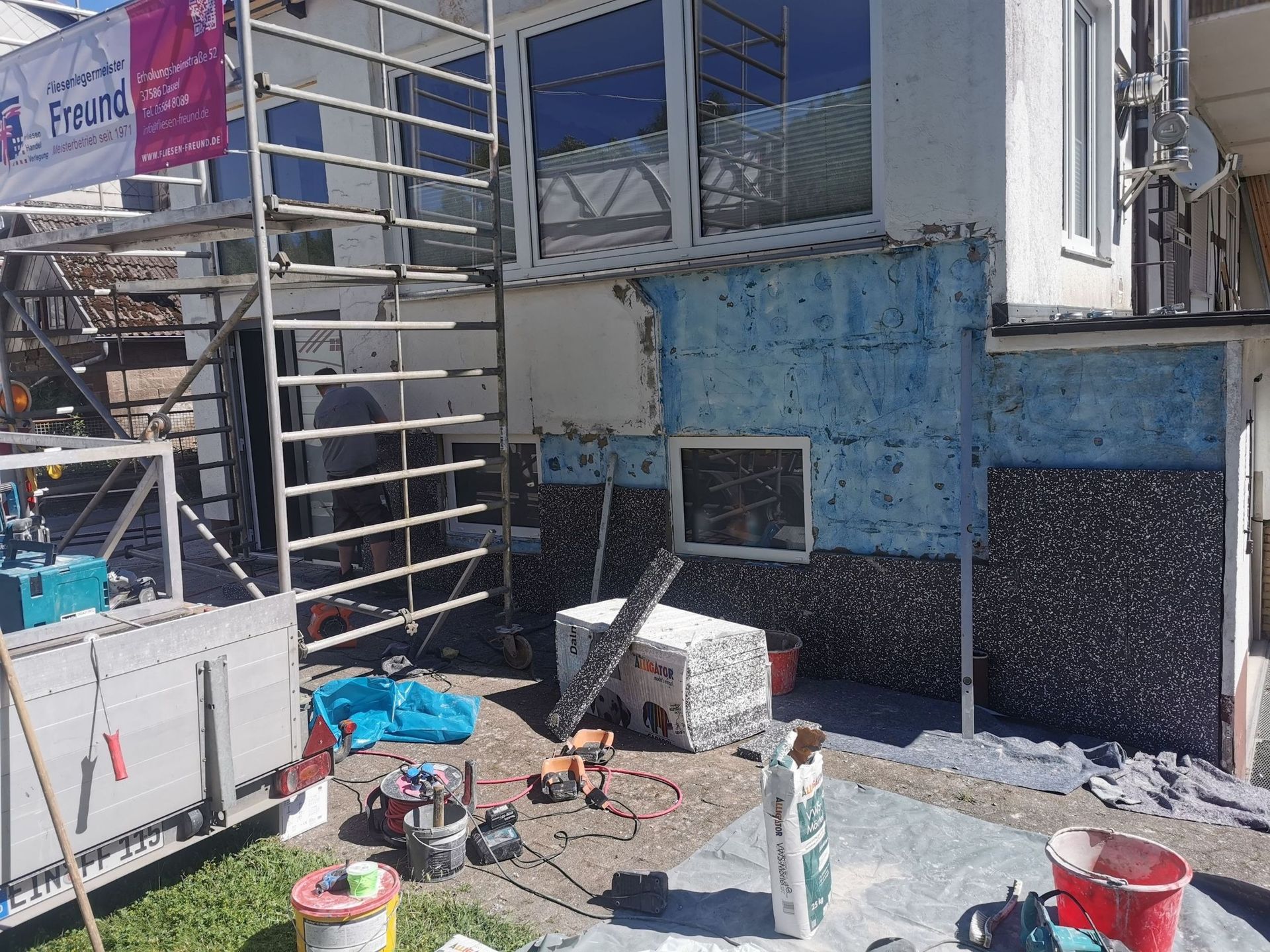 Fassadensanierung mit sichtbarem Gerüst, Werkzeugen und Baumaterialien. Blaue und graue Fassade.