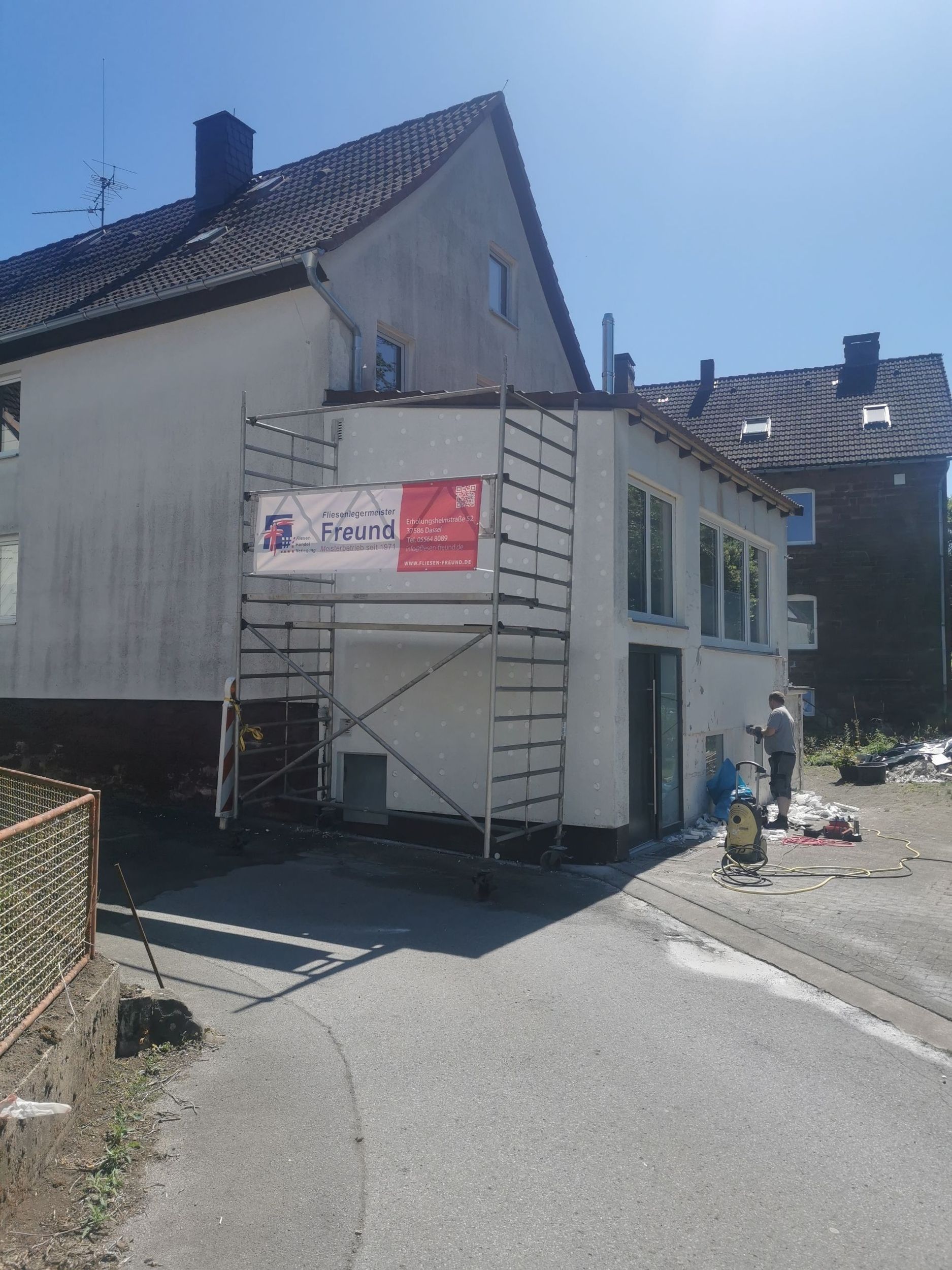 Baugerüst an weißem Gebäude mit Banner, Bauarbeiten im Gange. Sonniger Tag.