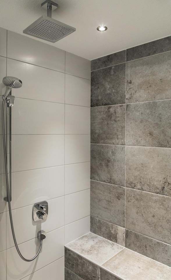 Dusche mit grau-weiß gefliesten Wänden, Decken- und Handbrause sowie eingebauter Sitzbank.