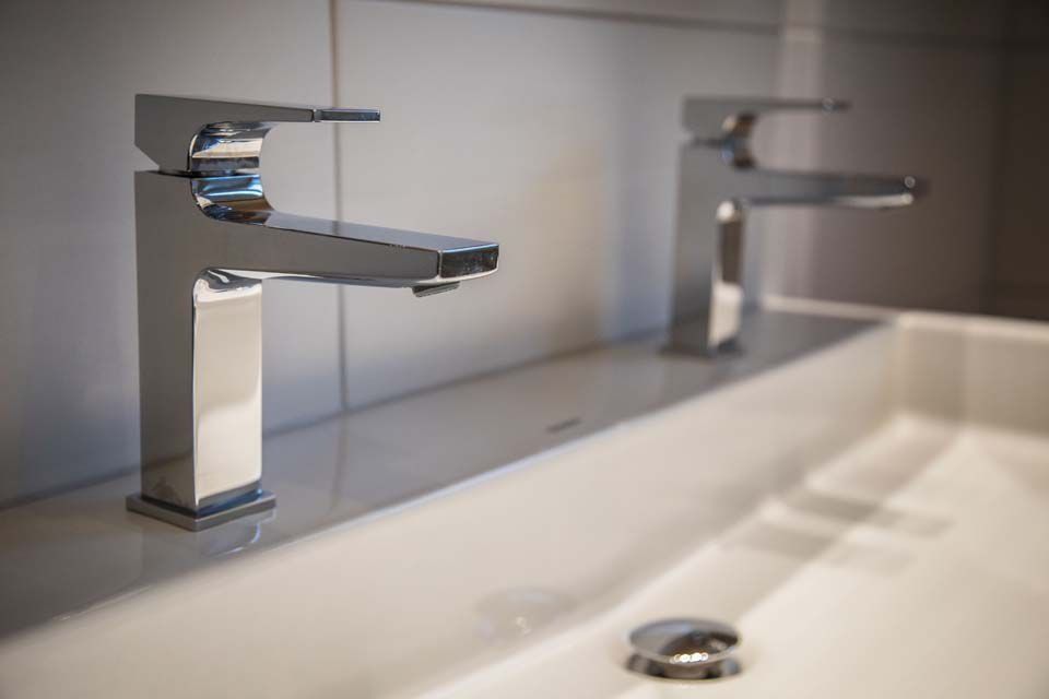 Zwei moderne, verchromte Badezimmerarmaturen über einem weißen Waschbecken.