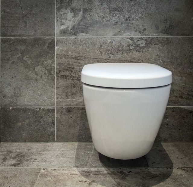 Weiße, wandhängende Toilette vor grauer Steinfliesenwand in einem Badezimmer.