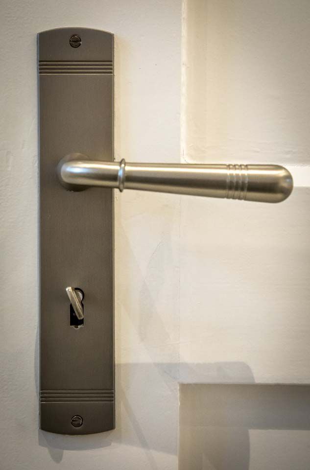 Silberner Türgriff an einer weißen Tür. Der Griff hat ein Schlüsselloch und eine strukturierte Rosette.