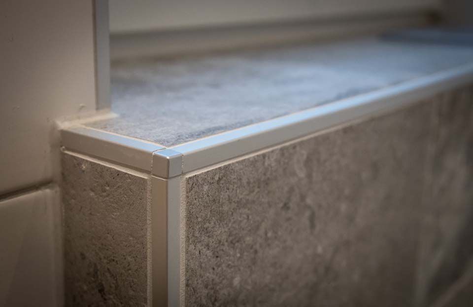 Arbeitsplatte und Wand aus grauen Fliesen mit silberner Umrandung.