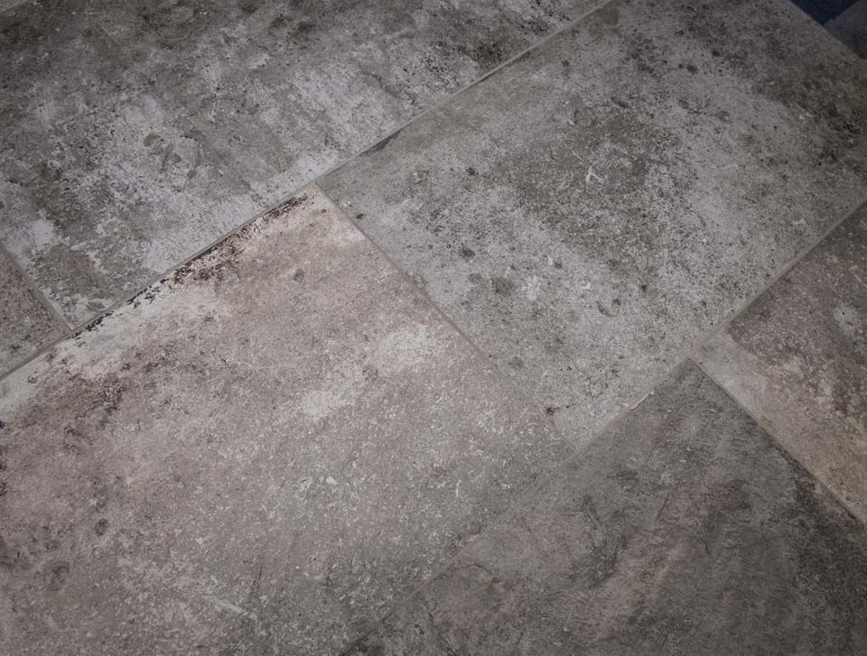 Graue, strukturierte Steinfliesen auf einem Boden, mit sichtbaren Fugen und Abweichungen in Farbe und Muster.