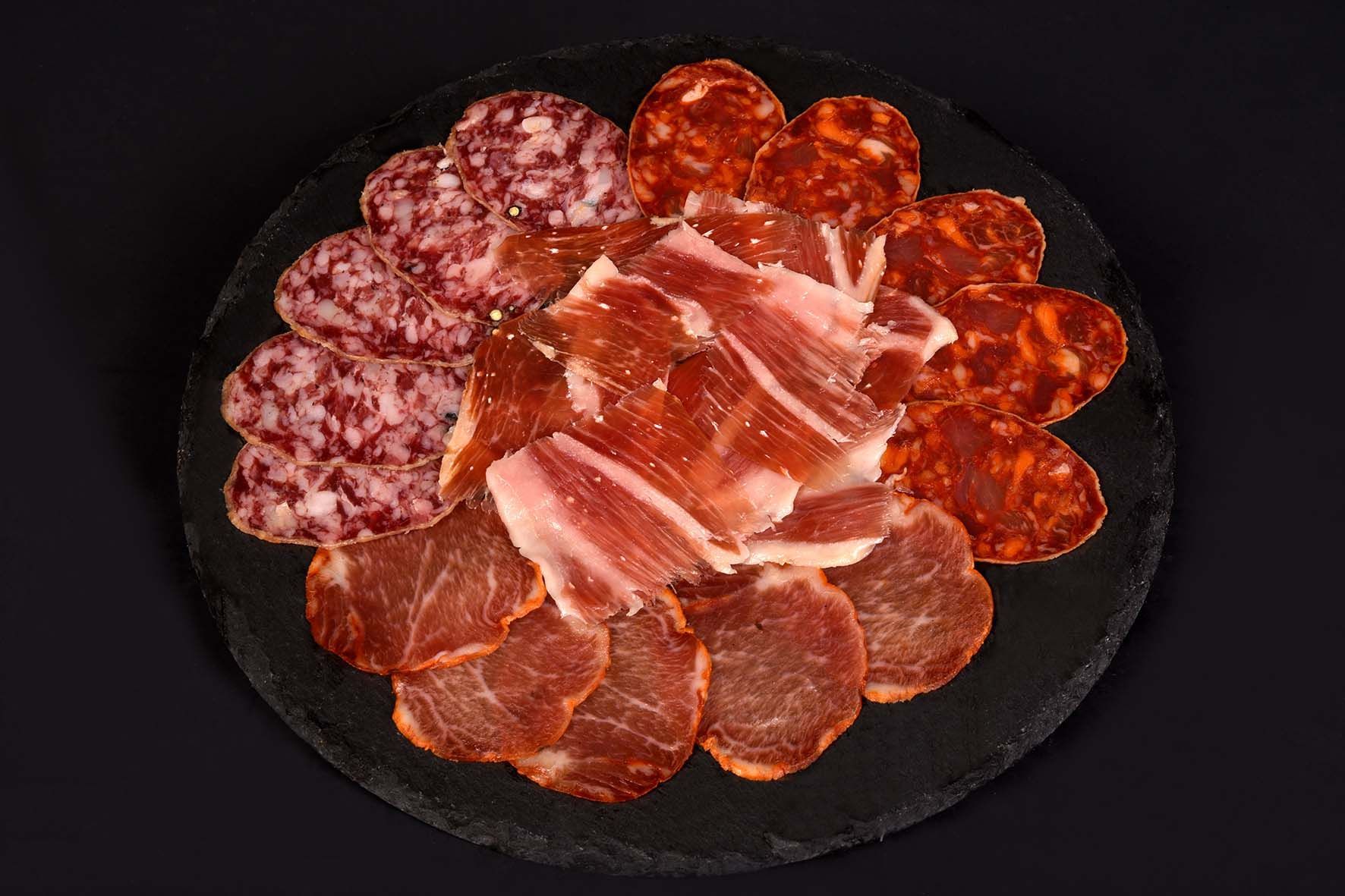 Plato de embutidos con salami en rodajas, chorizo, jamón y lomo de cerdo en un plato negro.