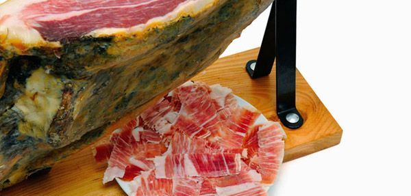 Un jamón curado cortado en lonchas sobre una tabla de madera con soporte metálico de color negro.