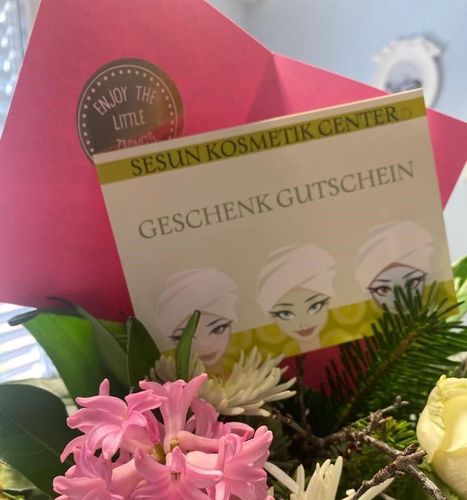 Eine Geschenkkarte vom Sesun Kosmetik Center ist von Blumen umgeben