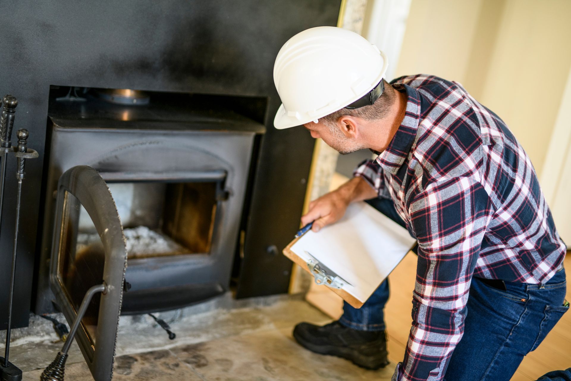 Un ouvrier portant un casque de chantier inspecte l'ouverture d'une cheminée à l'aide d'un bloc-notes à l'intérieur d'une maison
