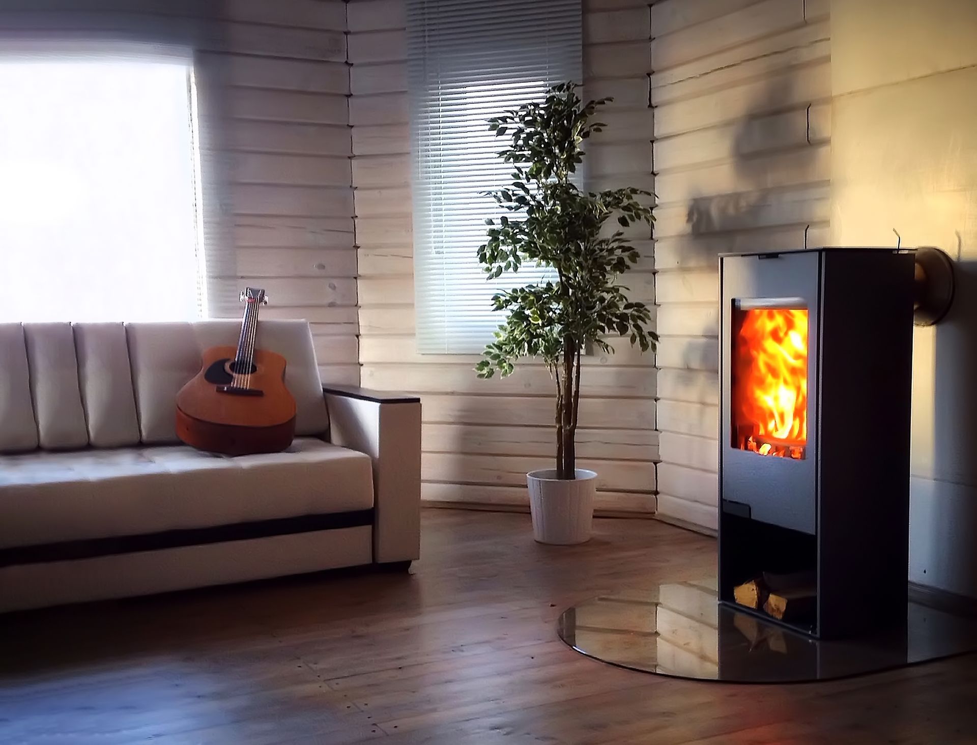 Salon chaleureux avec canapé, guitare, arbre en pot et cheminée moderne illuminée sur un parquet.