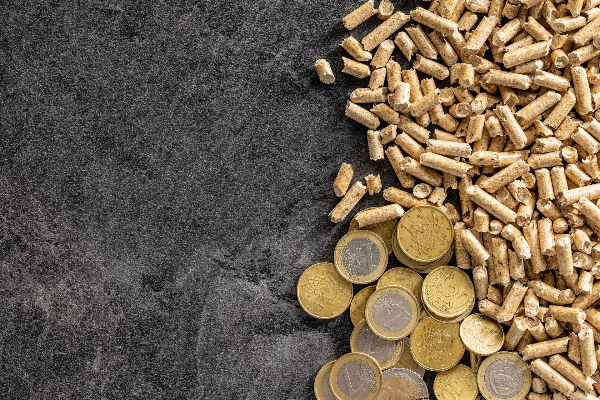 Des granulés de bois et des pièces d'or regroupés sur une surface sombre et texturée, évoquant un concept d'économie de carburant ou d'argent