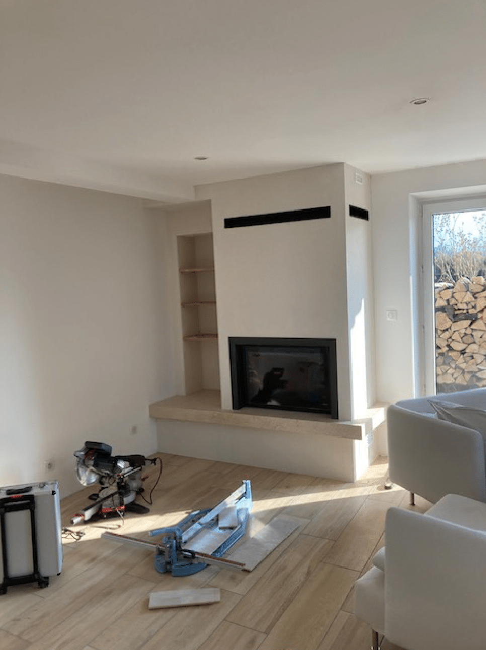 Salon lumineux avec cheminée, grandes fenêtres et outils au sol pendant les travaux de rénovation