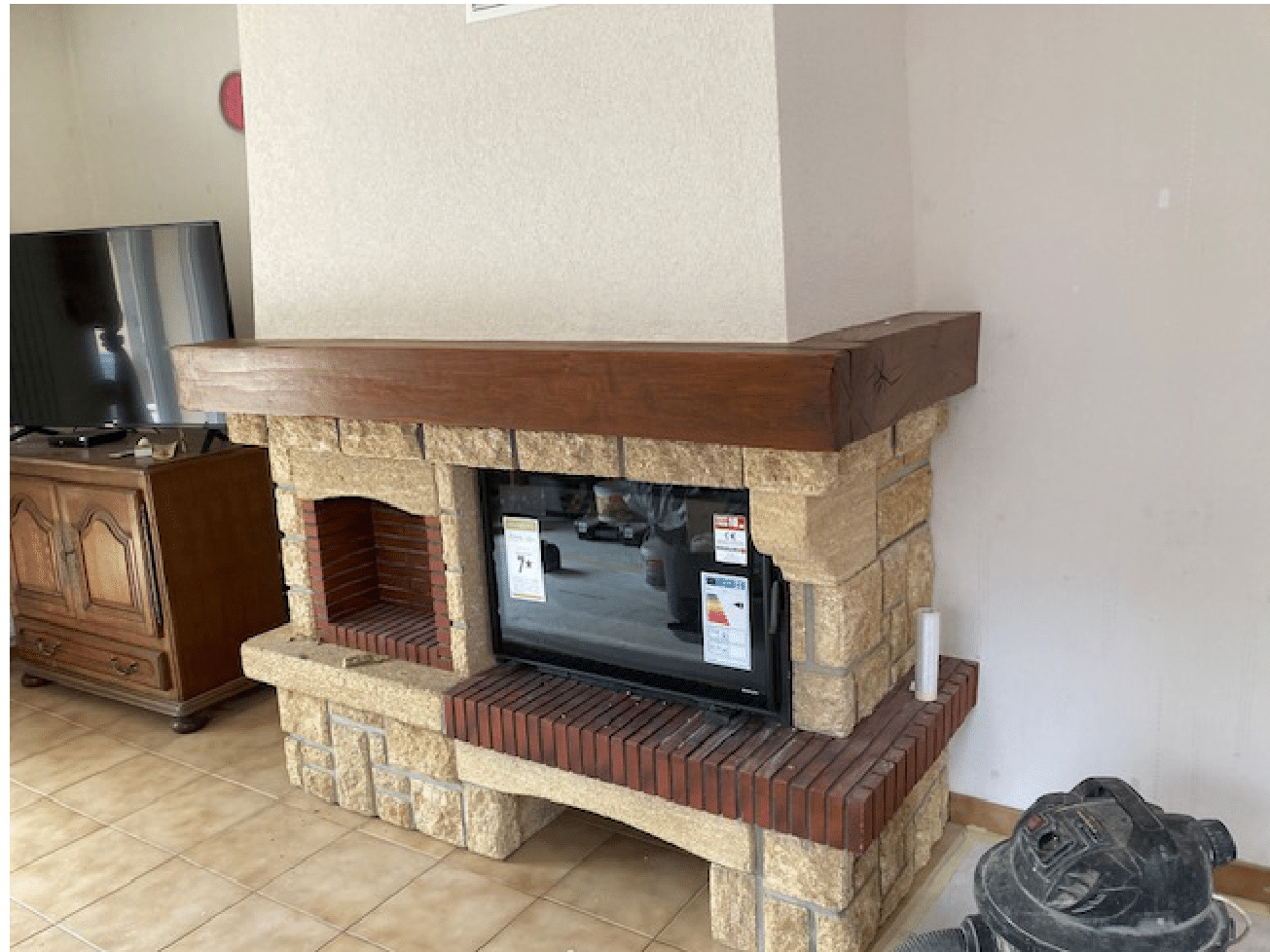 Cheminée en pierre et en bois avec insert TV, adossée à un mur clair dans un salon.