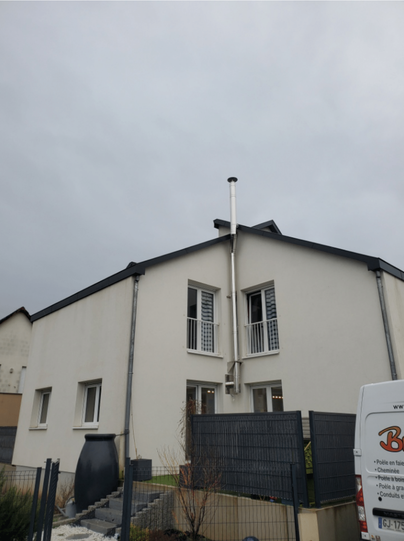 Maison blanche à deux étages avec une cour clôturée sous un ciel nuageux
