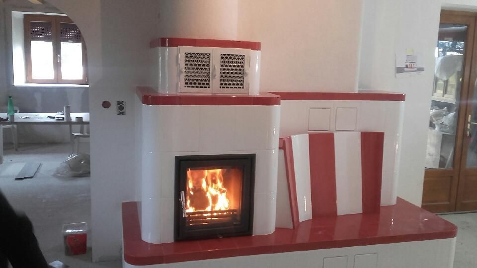 Cheminée blanche aux encadrements rouges et feu crépitant dans une pièce chaleureuse, avec des chaises rouges et blanches à côté.