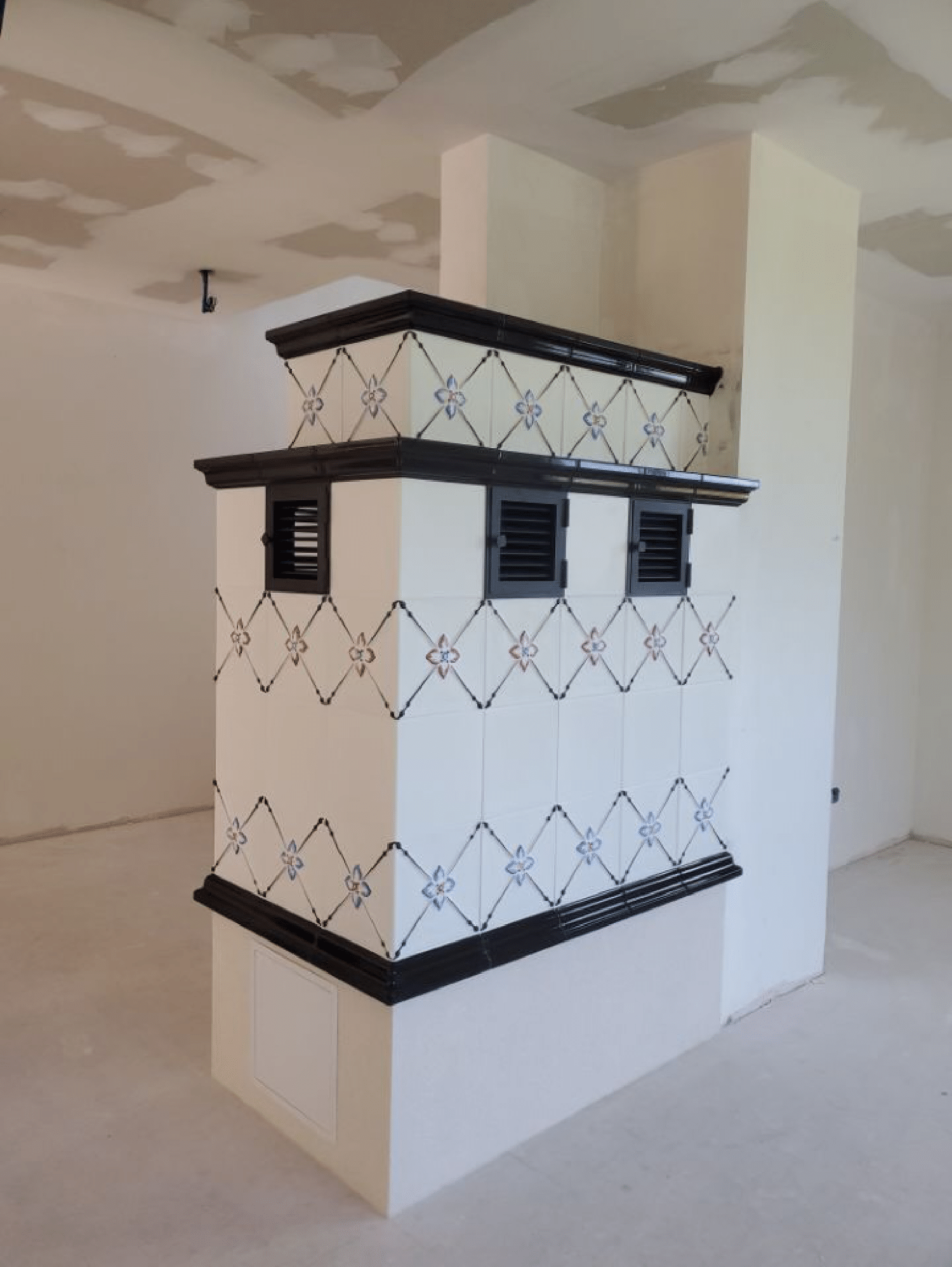 Poêle ou colonne de ventilation carrelée de blanc avec garniture noire et treillis métallique à losanges dans une pièce non finie