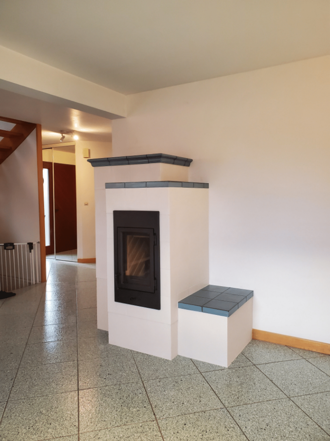 Salon avec cheminée ou poêle blanc, sol carrelé et escalier en arrière-plan