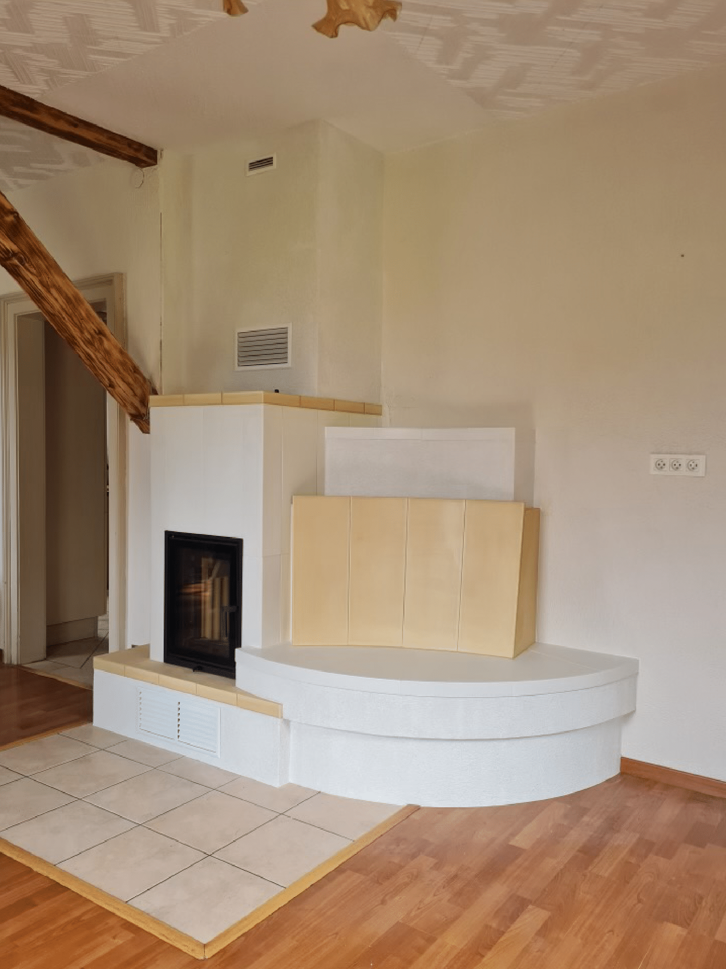 Salon vide avec une cheminée d'angle blanche et un foyer carrelé beige sur parquet.