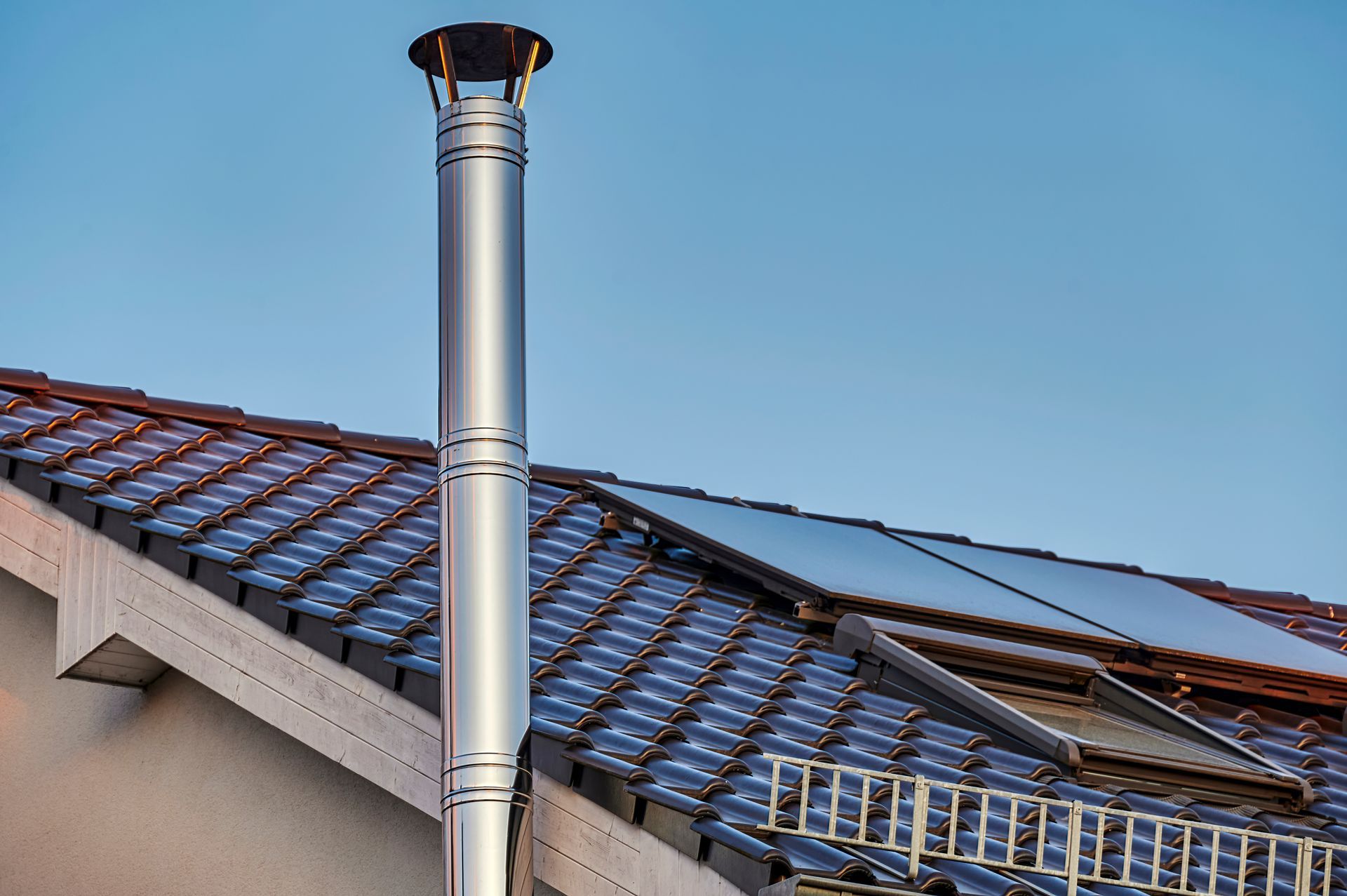 Cheminée métallique sur un toit de tuiles avec panneaux solaires sous un ciel bleu
