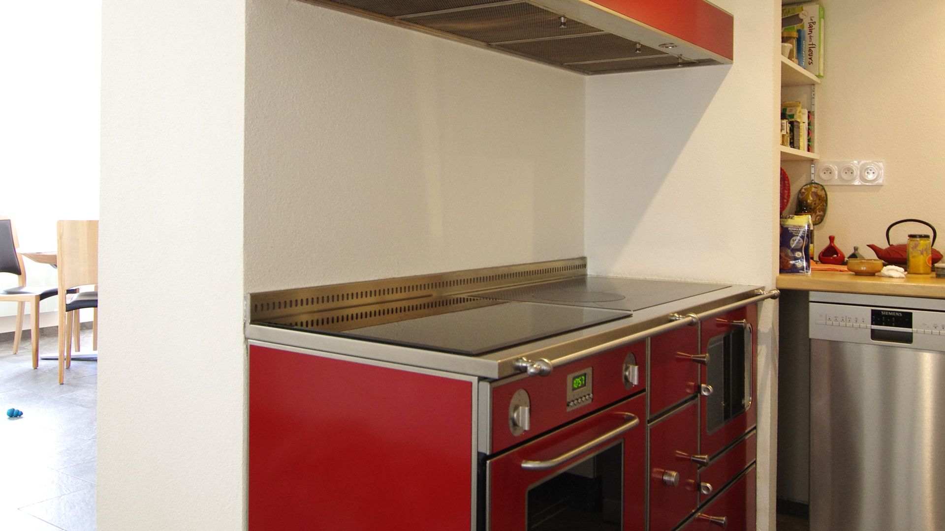 Cuisinière et plan de travail rouges sous un meuble blanc dans une cuisine lumineuse.