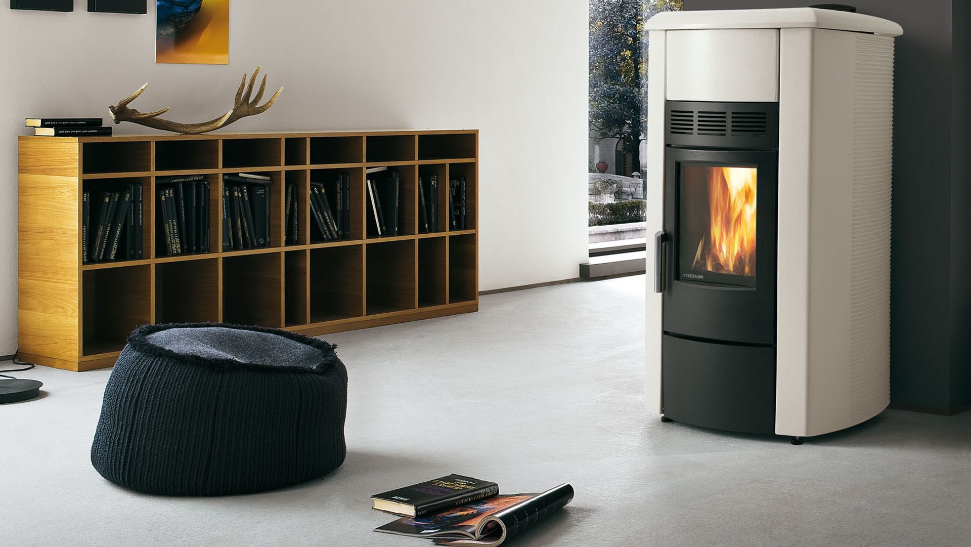 Salon moderne avec un poêle à bois blanc, une étagère basse, un pouf noir et des magazines au sol
