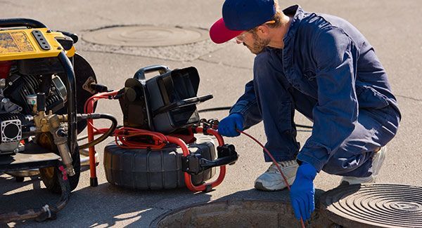 Un homme avec une casquette bicolore utilise un dispositif vidéo pour inspecter une canalisation