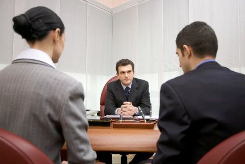 Tres profesionales vestidos de traje están sentados alrededor de un escritorio en una oficina para una reunión formal.