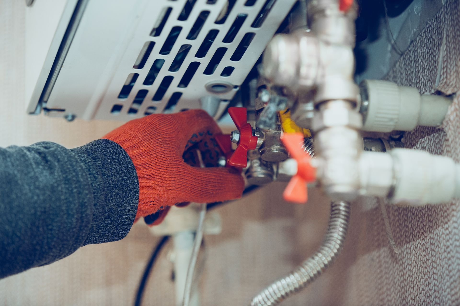 Une main gantée tourne une valve rouge sur un chauffe-eau à gaz.