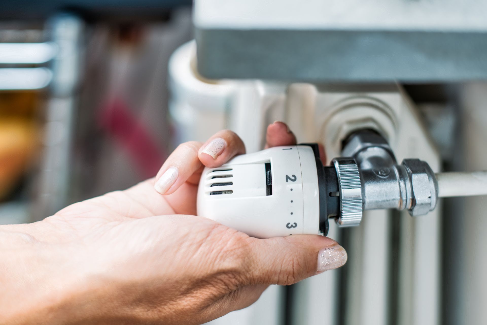 Main tournant un bouton de thermostat blanc sur un radiateur, le réglant sur 2.