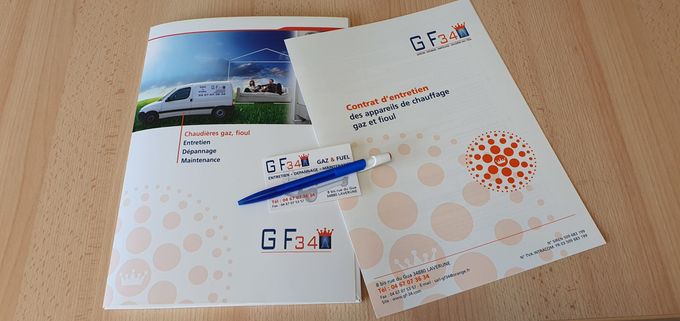 Brochures et stylo sur une surface en bois. Les brochures arborent un logo avec les lettres « G Fari ».