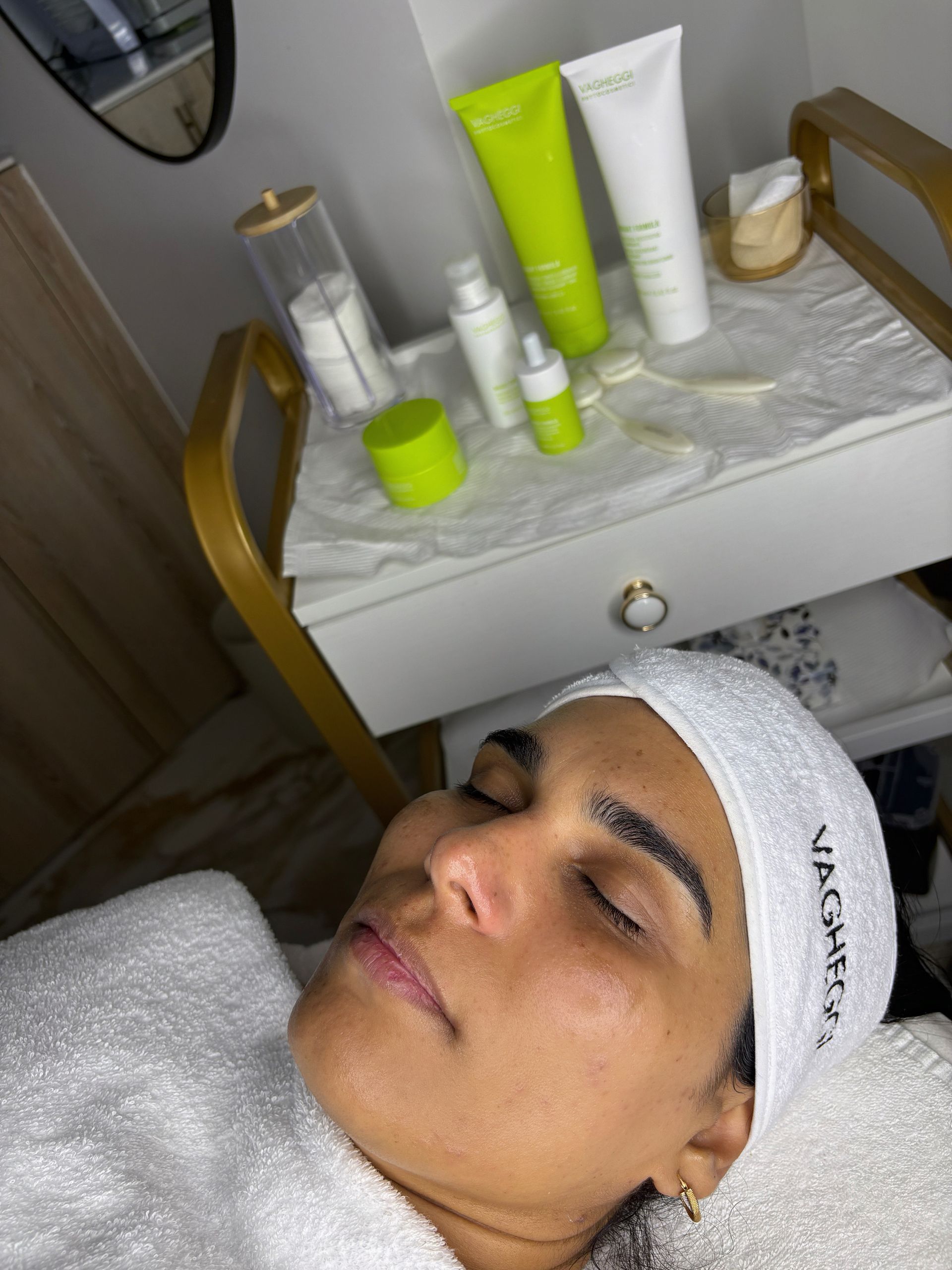 Mujer relajándose para un tratamiento facial, productos para el cuidado de la piel en una mesa cercana; entorno de spa.