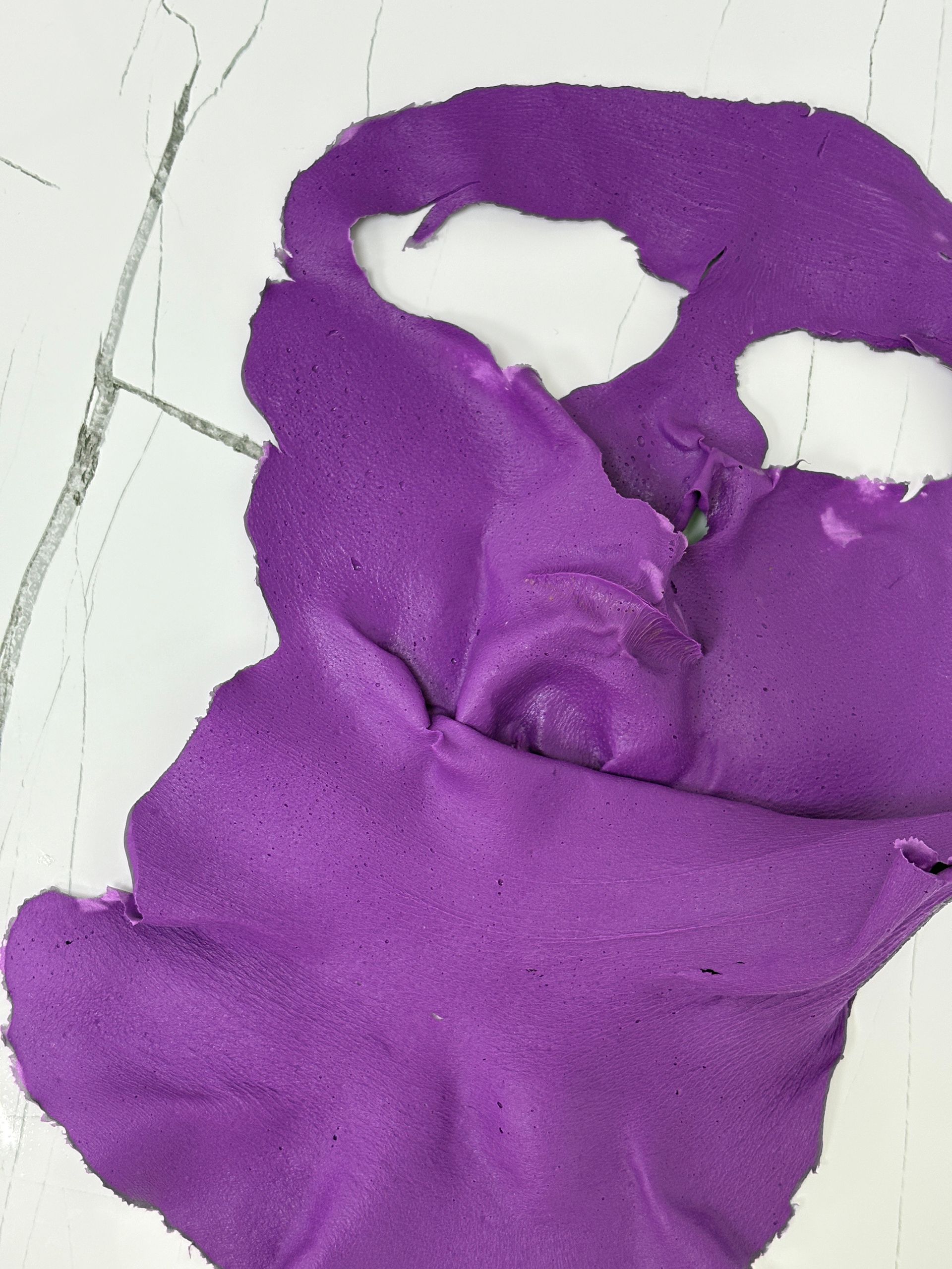 Mancha texturizada de color púrpura sobre una superficie blanca agrietada.
