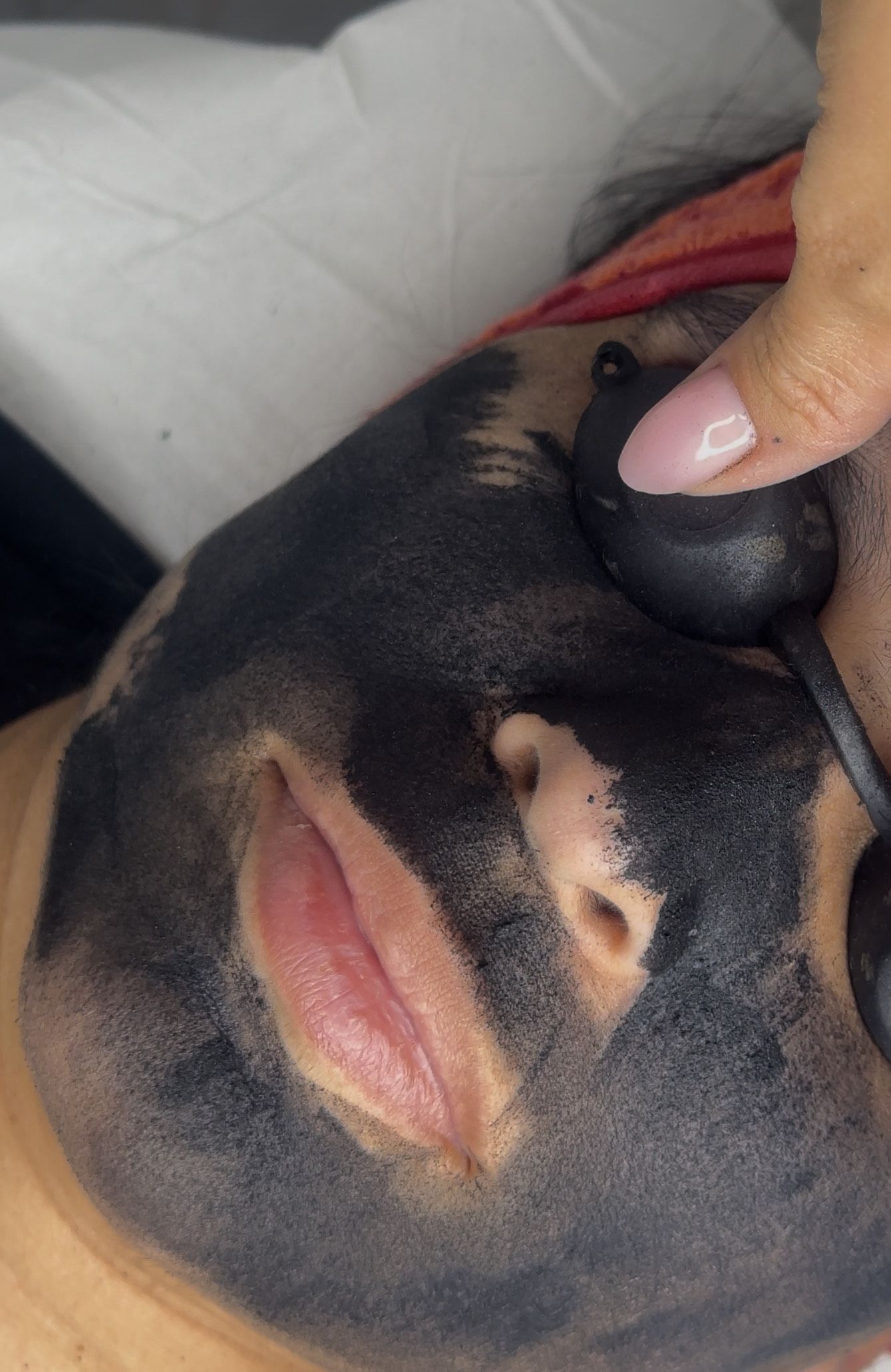 Persona con mascarilla de carbón negra y gafas protectoras. Una mano toca suavemente el rostro.