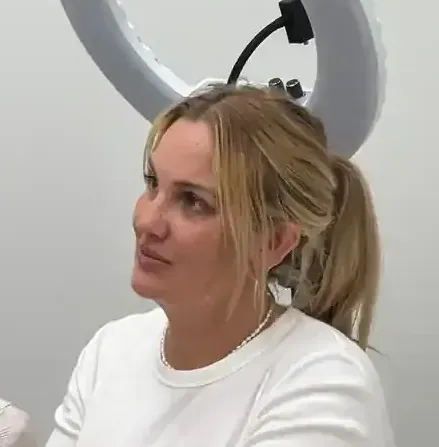 Una mujer con una camisa blanca está sentada frente a un anillo de luz.
